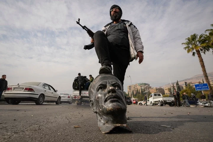 An opposition fighter steps on a broken bust of Hafez