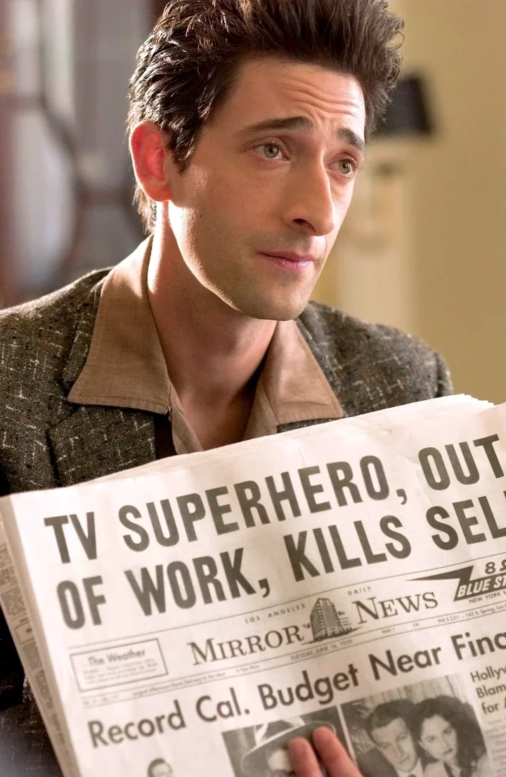 A person holding a newspaper with the headline &quot;TV Superhero, Out of Work, Kills Self.&quot;