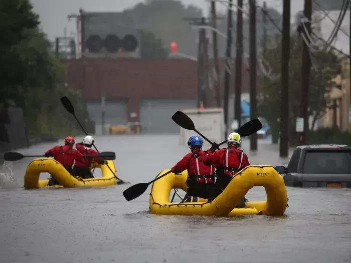 People in red jackets on yellow inflatable boats paddling down flooded streets