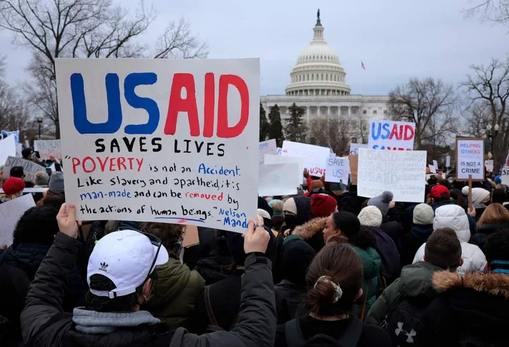 A crowd of protesters holding placards reading 'USAID Saves Lives