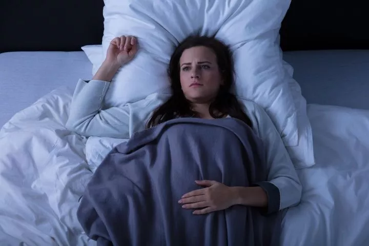 Young woman laying in bed awake in the dark