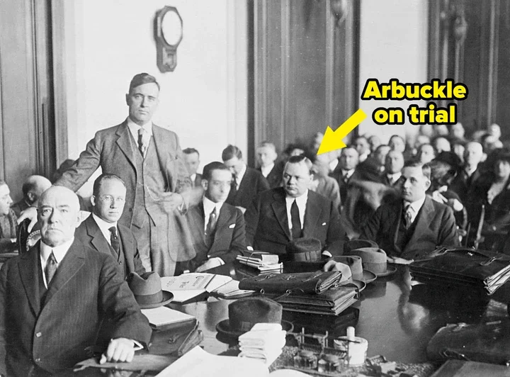 A historic courtroom scene with well-dressed men seated in suits, indicating a trial or legal proceeding from the early 20th century