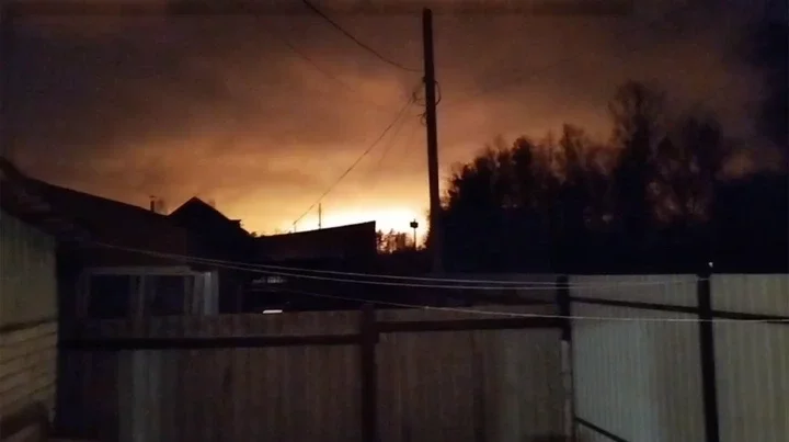 Nighttime view of a large fire or explosion in the distance.