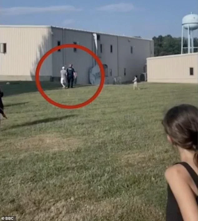 A member of the public is seen talking with a police officer before the shots rang out, the building where Crooks was perched is to the right