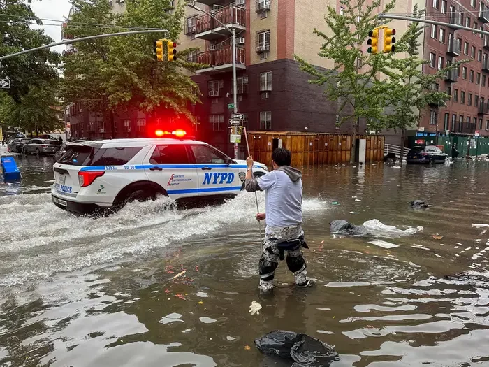A blue and white police van drives through brown water as a person rakes the ground