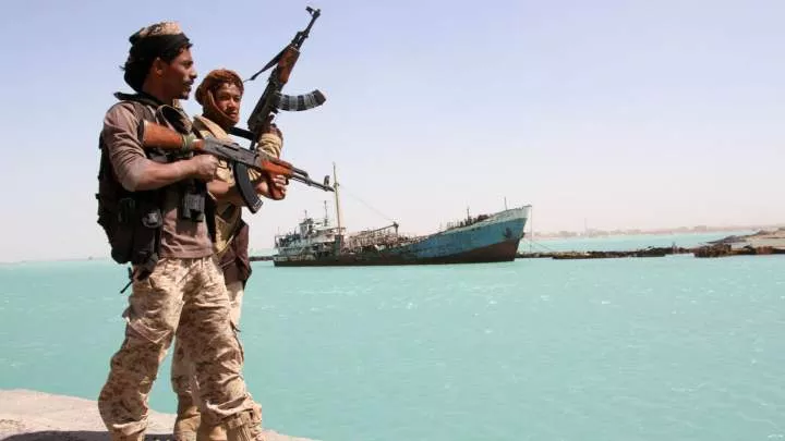 Armed Houthi rebels look out over the Red Sea where a commercial ship is sailing