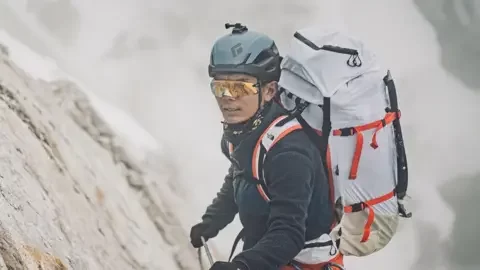 14 Peaks Expedition A man in climbing gear wearing a large backpack scales a cliff with a rope