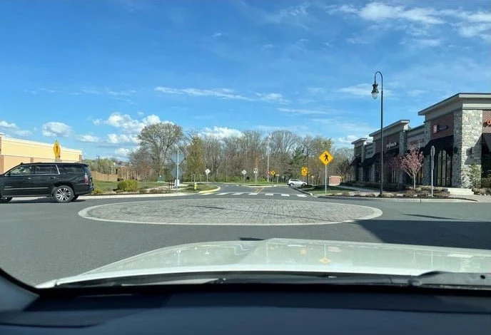 View from a car approaching a circular area laid with bricks in the middle of an intersection in a suburban commercial area