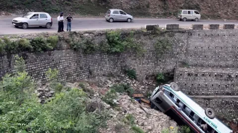 Reuters People look at the wreckage of a passenger bus after it skidded off a road on the outskirts of Jammu June 18, 2008. Two people were killed and 27 others injured in the accident, police said on Wednesday.
