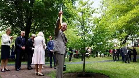 Reuters Britain's King Charles holds a shovel as he participates with Queen Camilla in a ceremonial tree planting next to Canada's Prime Minister Mark Carney as they visit the Rideau Hall residence during a two-day visit in Ottawa, Ontario, Canada May 26, 2025.