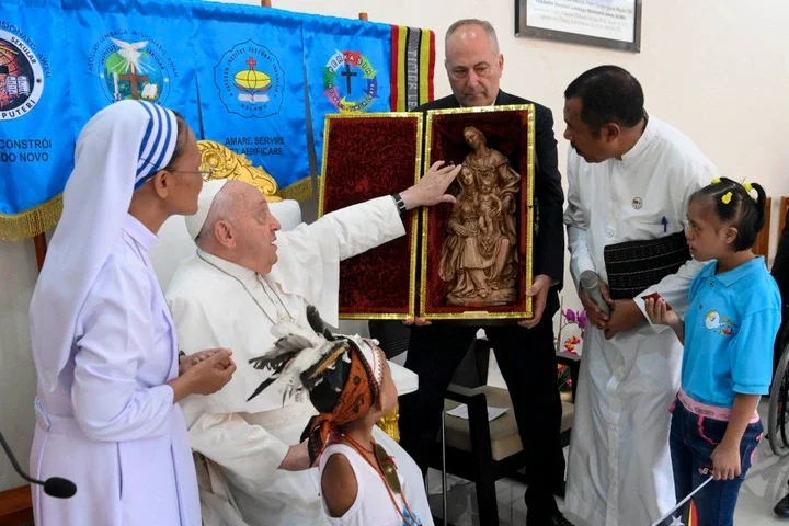 Pope Francis (C) touches a statue during a visit for children with disabilities at the Irmas Alma school in Dili.