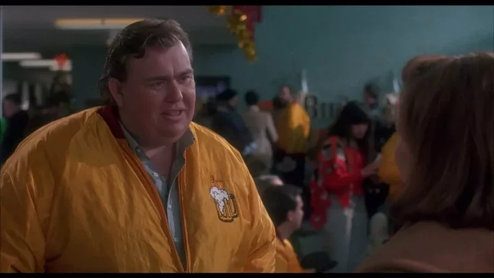 John Candy in character in Home Alone, wearing a yellow bomber jacket