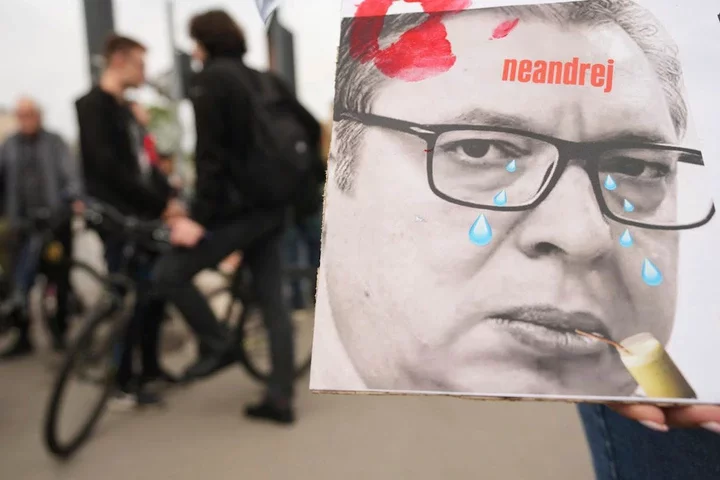 A woman holds a poster that shows Serbian President Aleksandar Vucic during a farewell ceremony for Serbia's protesting students, embarking on 2,000-kilometer (1,200-mile) run to Brussels aimed to draw European Union attention to their months-long struggle against corruption and for the rule of law in Novi Sad, Serbia, Friday, April 25, 2025. (AP Photo/Darko Vojinovic)