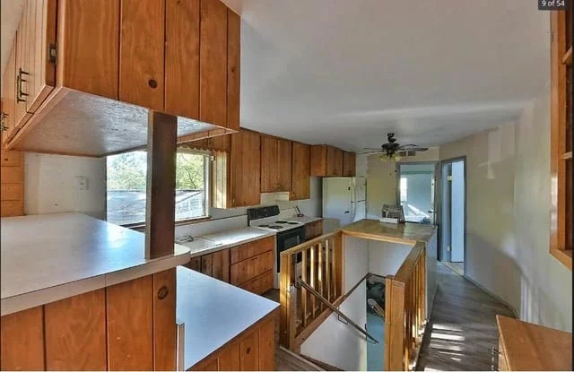 Kitchen with wooden cabinets. A stairwell opens in the middle of it, partially covered by a kitchen island