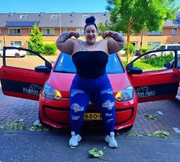 Jackie Koorn flexes her muscles in front of a car