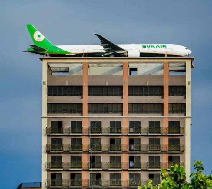 A Large Airplane Passing Behind A Building During Landing/Take-Off Looks Like It Is Parked On Top Of The Roof Of This Building