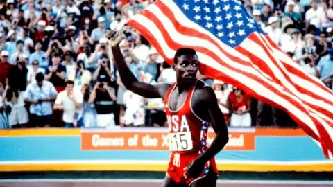 Getty Images Carl Lewis holds a US flag on the athletics track