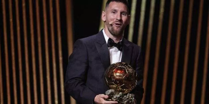 Lionel Messi in a black suit with the ballon d'or award for the best men's player of the year in his hands