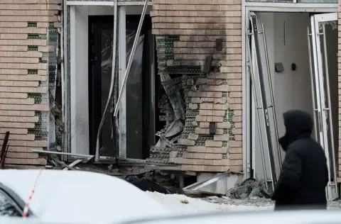 EPA Damage to brickwork and windows is seen on the outside of an apartment block in Moscow as a person in a hooded jacket looks on, taken 17 December.