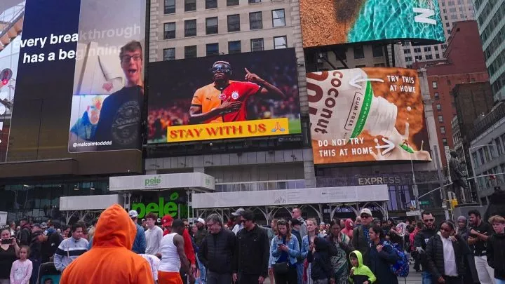 A billboard bearing a picture of Victor Osimhen and a message saying 'stay with us' is seen among other electronic advertising hoardings above a crowded street in New York