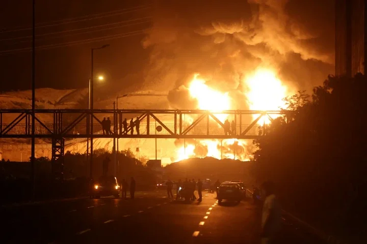 Reuters People watch from a bridge as flames from an Israeli attack rise from Sharan Oil depot