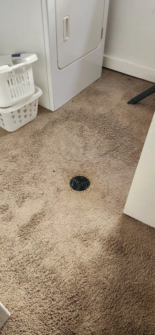 Carpeted laundry room floor with a drain in the middle