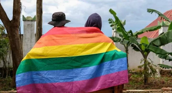 A gay Ugandan couple cover themselves with a pride flag as they pose for a photograph in Uganda Saturday, March 25, 2023.AP Photo