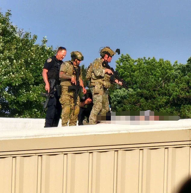 Police personnel standing over the body of the shooter on the rooftop