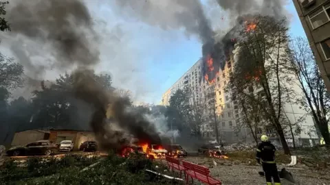 Reuters A firefighter looks at an apartment building and cars which burn after a Russian air strike in Kharkiv, Ukraine