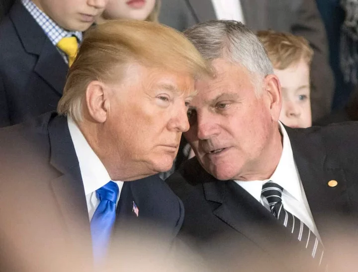 Two white men hold their heads together in quiet discussion.