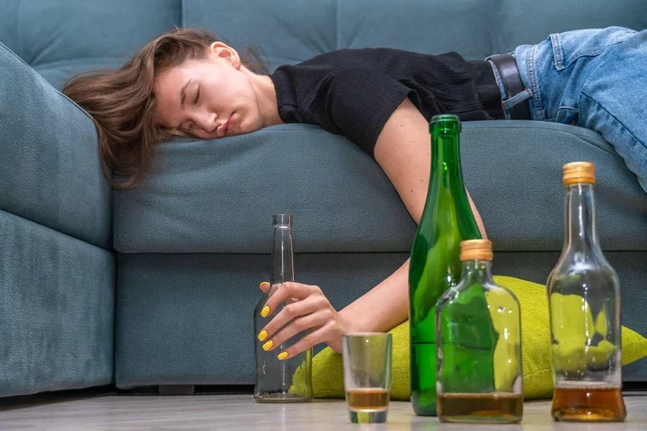 Tired young dark-haired woman lying on the couch after a party at home close-up, next to empty bottles on the floor